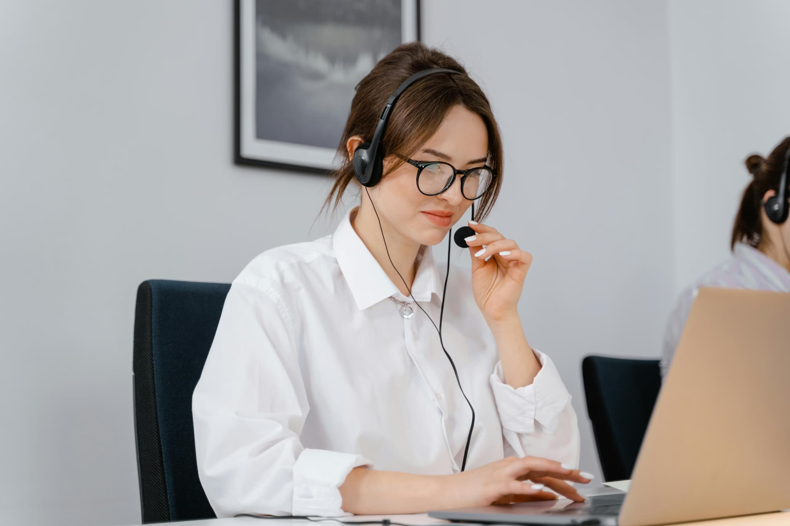 Photo of a woman in a white shirt holding the microphone on her headset