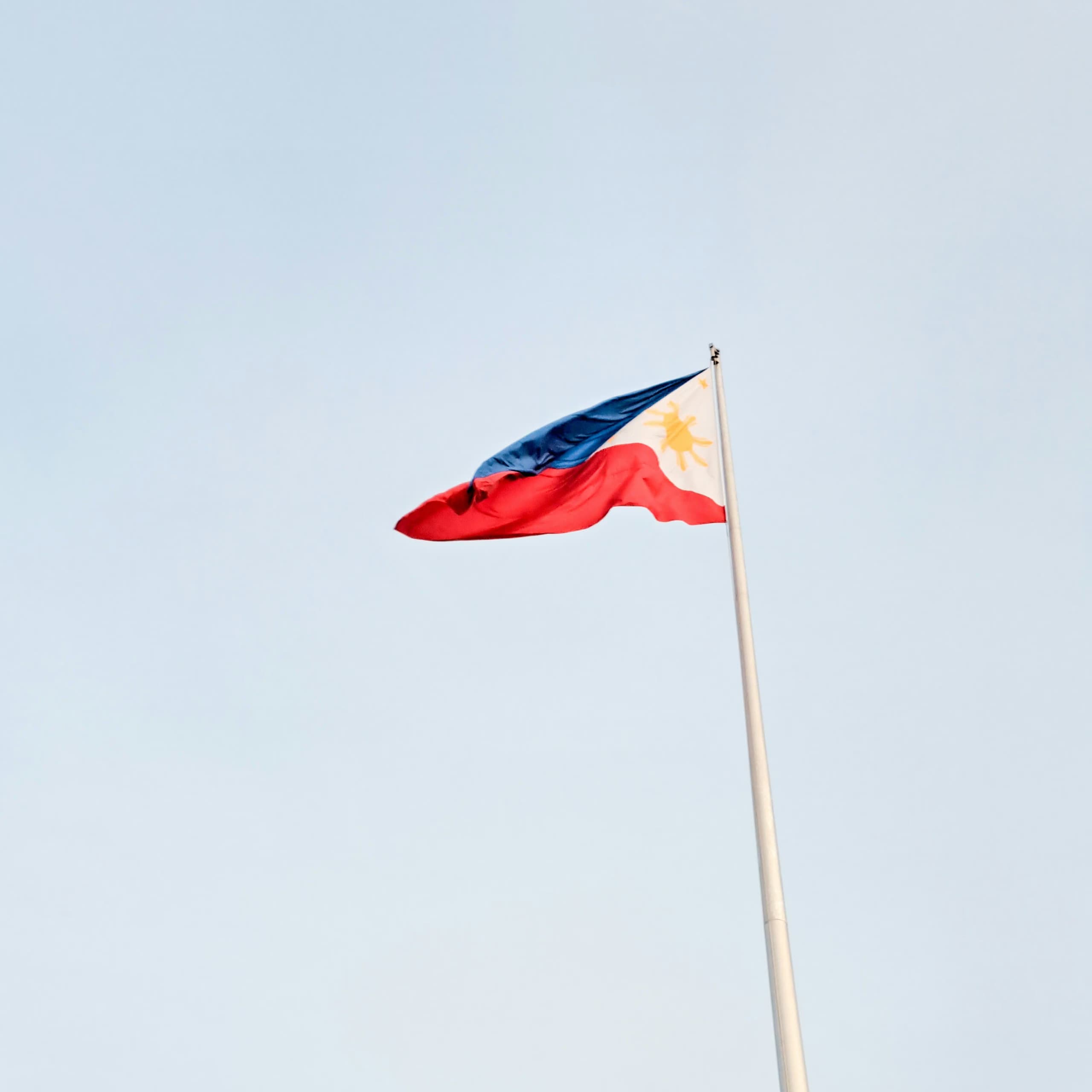 Capture the essence of Filipino pride with this stunning image of the Philippine flag dancing gracefully in the wind against a backdrop of clear blue skies.