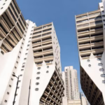Vue d'en bas de bâtiments modernes blancs aux formes géométriques complexes et balcons, sous un ciel bleu clair.